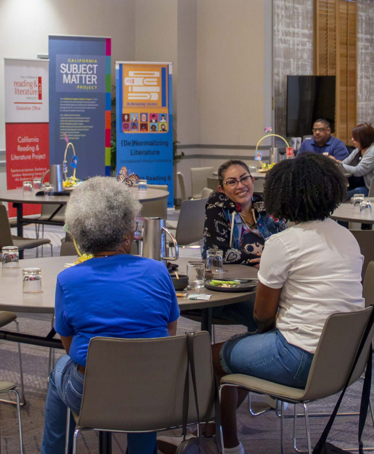 A group of women sit at a table smiling and talking during a CRLP open program.