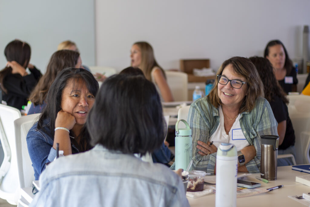 A group of women sit at a table smiling and talking during a CRLP event