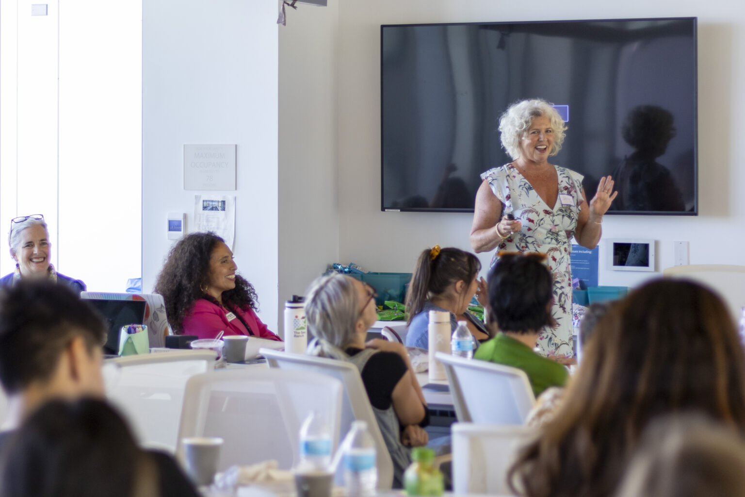 A woman in a floral dress presents to a group of adult learners