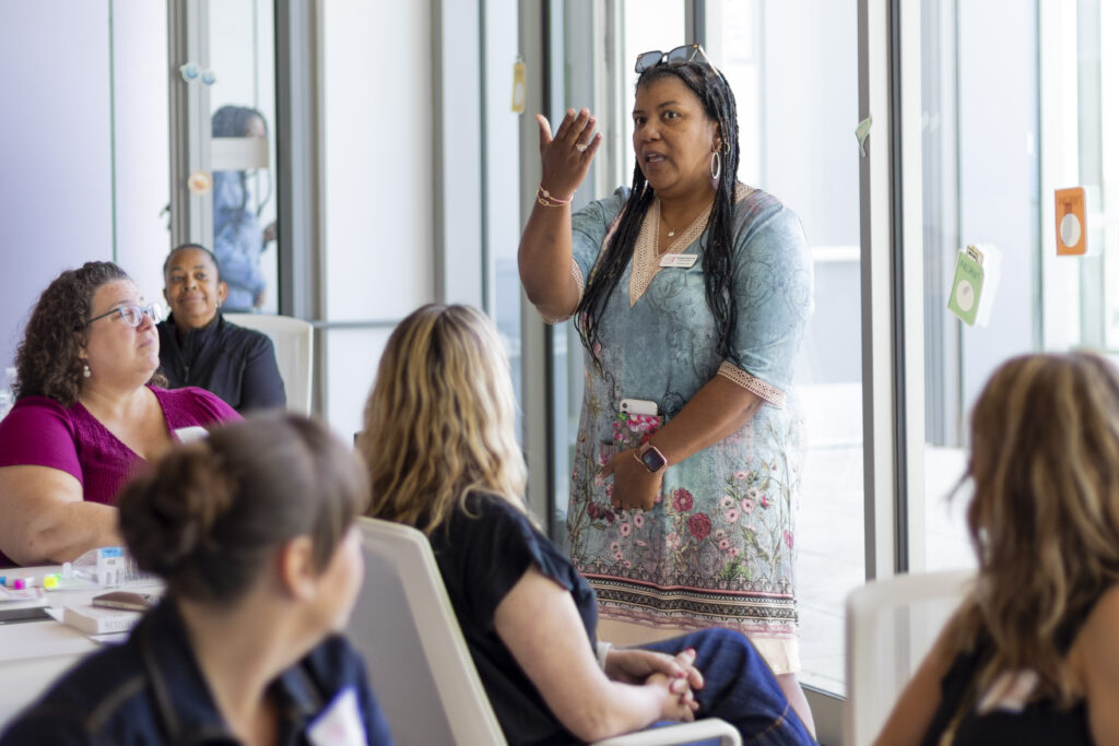 A woman in a blue dress presents to a group of adult learners